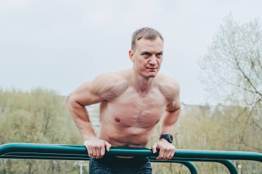 Fitness, spor, egzersiz, eğitim ve yaşam tarzı konsepti - yaz parkında paralel barlarda abdominal egzersiz yapan genç adam