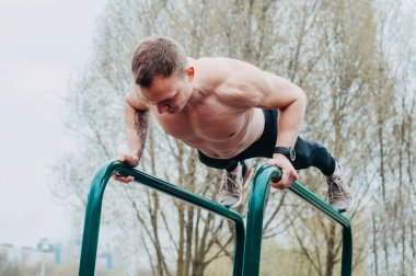 Fitness, spor, egzersiz, eğitim ve yaşam tarzı konsepti - yaz parkında paralel barlarda abdominal egzersiz yapan genç adam