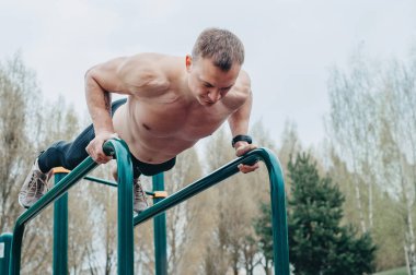 Fitness, spor, egzersiz, eğitim ve yaşam tarzı konsepti - yaz parkında paralel barlarda abdominal egzersiz yapan genç adam