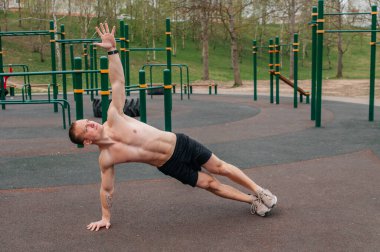 Çıplak gövdeli ve siyah şortlu genç bir adam spor sahasının kenarındaki barda duruyor.