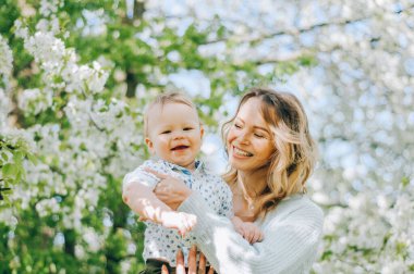 Uzun kıvırcık saçlı anne parkta oğluyla oynuyor. Mutlu aile, doğada rahatlayıp hayatın tadını çıkarıyor. Açık hava çekimi. Kopyalama alanı