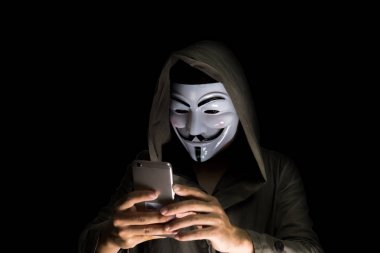 Bir hacker bir bornoz giymiş bir maske takıyor. Smartphone hırsızlığı kullanarak ve siber verilere saldıran. Siyah arka plan ve kırpma yolu izole.