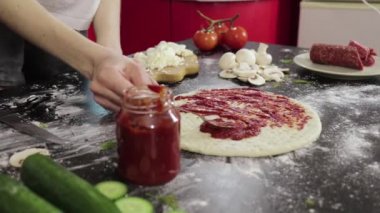 Genç bir kızın elleri pizza hamuruna domates ezmesi sürüyor.
