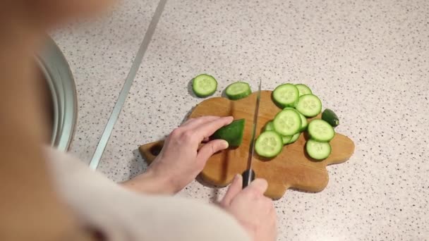 Handen van een jong meisje gesneden een komkommer op een houten plank close-up — Stockvideo