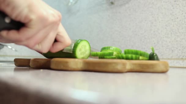 As mãos de uma menina jovem cortam um pepino em uma tábua de madeira de perto — Vídeo de Stock