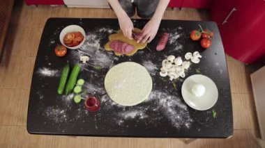 Siyah masada kör bıçakla sosis kesen genç bir kızın elleri. Hazır pizza.