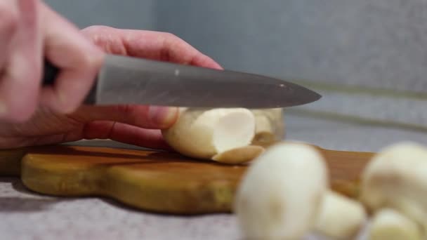 Las manos de una joven cortan un hongo en la tabla de cortar de madera, fondo claro, de cerca — Vídeo de stock