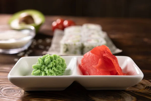 Beyaz bir tabakta wasabi ve zencefil ve bulanık bir arka planda rulo
