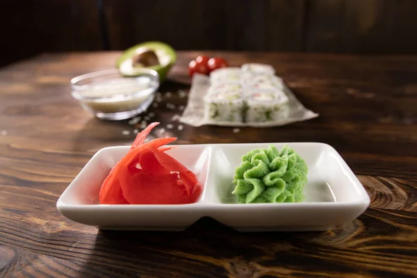 Beyaz bir tabakta wasabi ve zencefil ve bulanık bir arka planda rulo