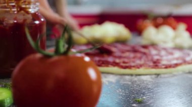 Genç kızın elleri pizza hamuruna domates ezmesi sürüyor.