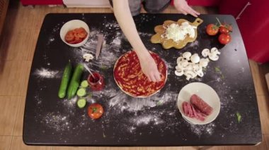 Genç kızın elleri pizza hamuruna domates koyuyor.