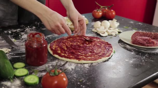 Χέρια της νεαρής κοπέλας πασπαλίζουν πελτέ ντομάτας σε ζύμη πίτσα — Αρχείο Βίντεο