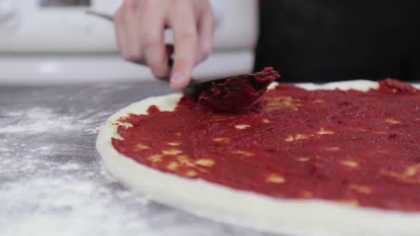 Genç bir adamın elleri pizza hamuruna domates ezmesi sürüp sürüyor. — Stok video