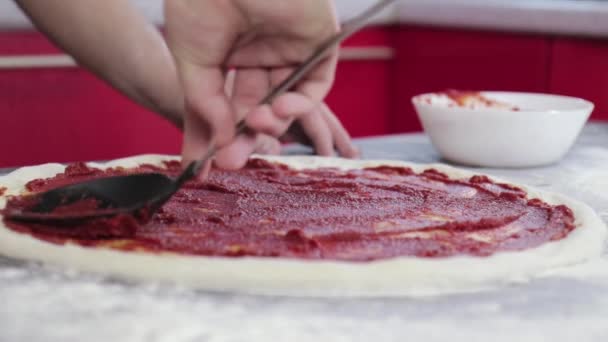 Genç bir adamın elleri pizza hamuruna domates ezmesi sürüp sürüyor. — Stok video