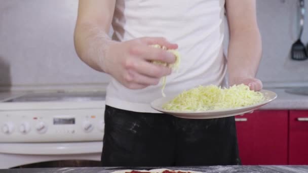 Hands of man sprinkle cheese on dough for pizza with tomato paste — Stock Video