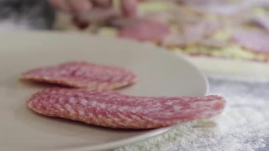 Genç adamın elleri pizza hamurunun üzerine sosis koyar.