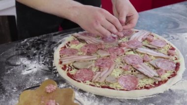 Genç adamın elleri pizza hamurunun üzerine sosis koyar.