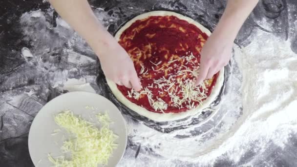 Handen van de mens bestrooi kaas op deeg voor pizza met tomatenpuree bovenaanzicht — Stockvideo