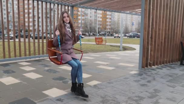 Gelukkig jong meisje swinging op een swing in het park met auto 's in de achtergrond — Stockvideo