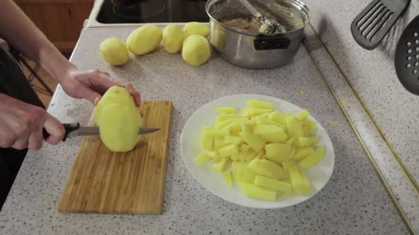 Las manos cortan las patatas en los trozos a la tabla de madera — Vídeos de Stock