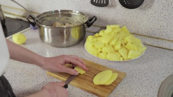 Las manos cortan las patatas en los trozos a la tabla de madera — Vídeo de stock