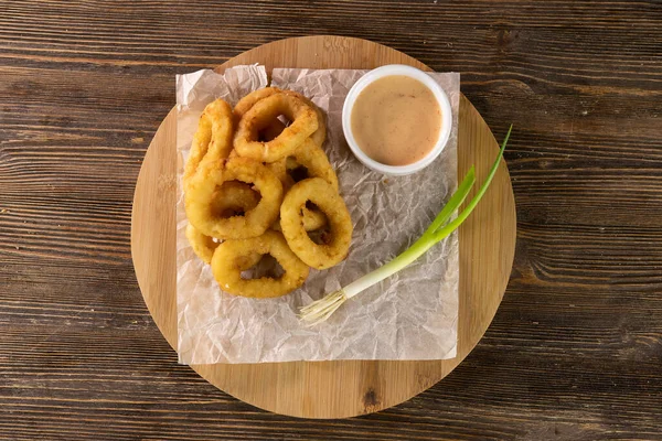 Anillos de cebolla frita con salsa y puerro verde en papel y círculo de madera vista superior —  Fotos de Stock