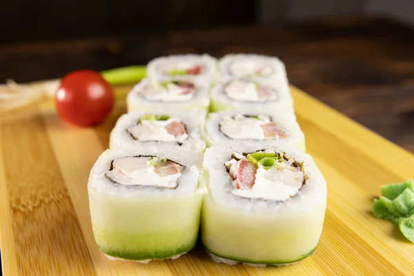 Suşi, salatalık, tavuk, yeşil pırasa ve domates ahşap tahtada wasabi manzaralı.