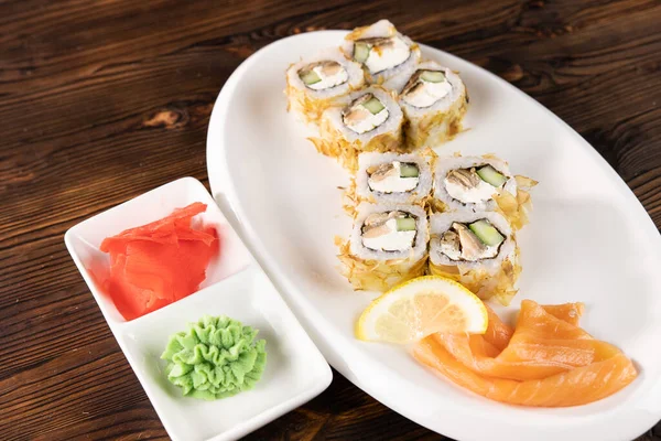 Oval tabakta somon, peynir ve avokado. Kare tabaklarda Wasabi ve zencefil. Koyu tahta masada.
