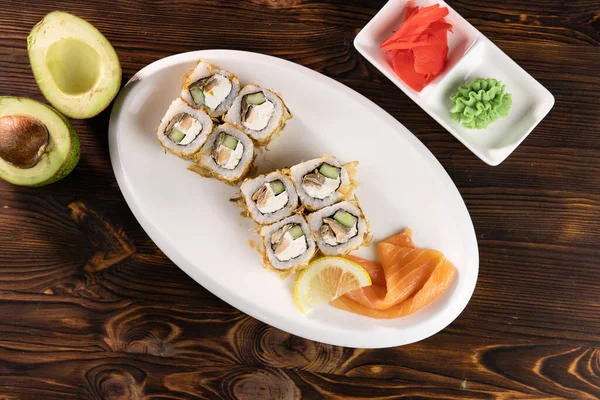 Oval tabakta somon, peynir ve avokado. Wasabi ve zencefil kare tabaklar üzerinde koyu ahşap masa üstünde.
