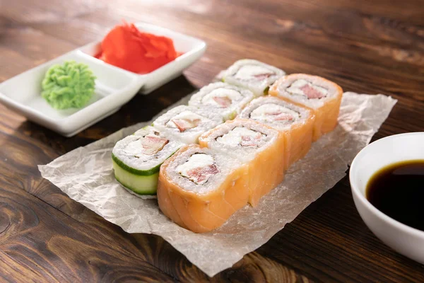 Kağıt üzerinde somon, domates, peynir ve salatalık. Wasabi ve zencefil kare tabakta, soya sosu koyu ahşap masada.