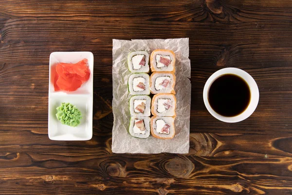 Kağıt üzerinde somon, domates, peynir ve salatalık. Wasabi ve zencefil kare tabakta, soya sosu koyu ahşap masa üstünde.