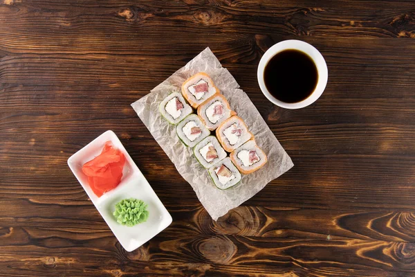 Kağıt üzerinde somon, domates, peynir ve salatalık. Wasabi ve zencefil kare tabakta, soya sosu koyu ahşap masa üstünde.