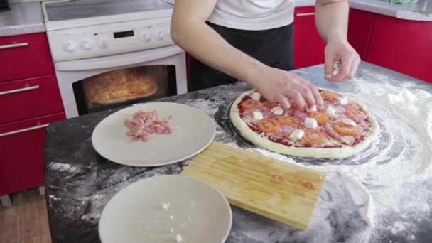 Мужчины руки положить сыр на пиццу с мясом и помидорами на стол с мукой. Домашняя пицца — стоковое видео