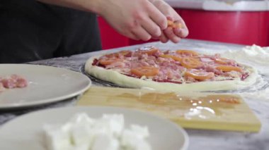 Adamın elleri pizza hamuruna domates ve peynir koydu.