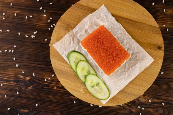 Avokado, kar yengeci ve kırmızı tobiko havyarı ve kağıt üzerinde dilimlenmiş salatalık ve ahşap yuvarlak tahta.