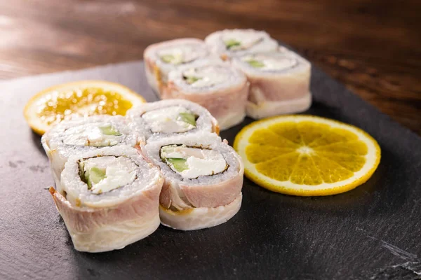 Pastırmalı suşi, avokado ve siyah Japon tabağında dilimlenmiş portakallı beyaz balık.