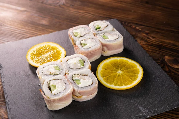 Pastırmalı suşi, avokado ve siyah Japon tabağında dilimlenmiş portakallı beyaz balık.