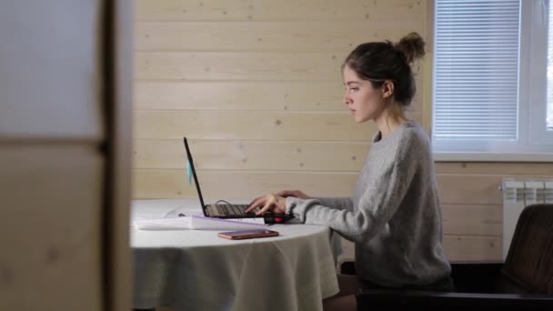 Chica joven trabaja en el ordenador portátil y se siente dolor de espalda en casa de madera — Vídeos de Stock