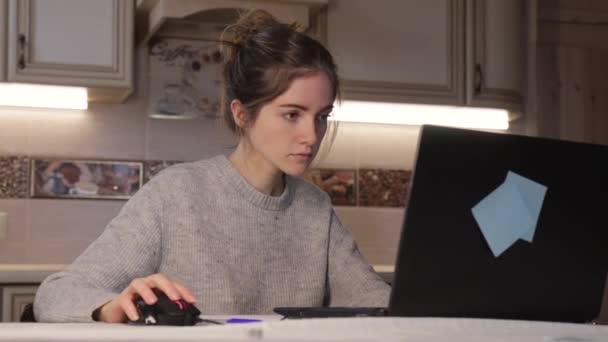 Молода дівчина працює на ноутбуці вдома ввечері. Дерев'яний фон — стокове відео