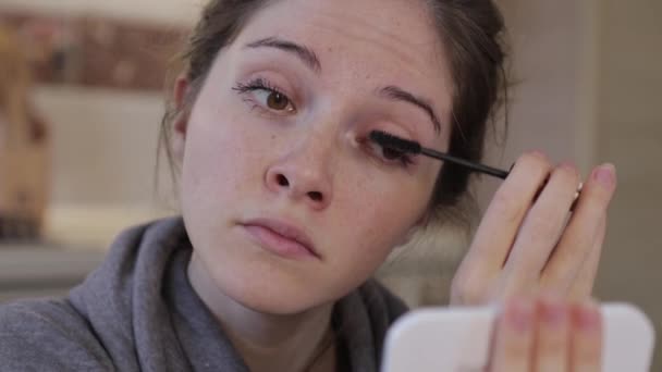 Flicka tittar i fickspegeln och bär mascara i hemmet, närbild — Stockvideo