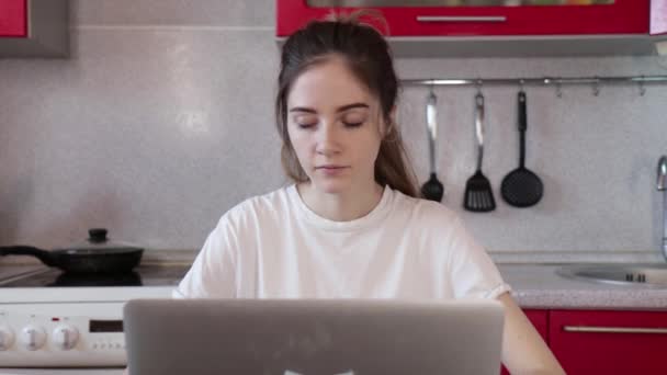 Το κορίτσι εργάζεται στο σπίτι σε ένα φορητό υπολογιστή, ακούει ένα τηλεφώνημα και απαντά — Αρχείο Βίντεο