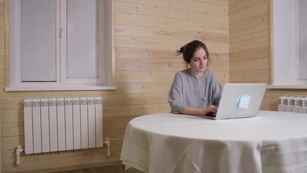 Menina em fones de ouvido funciona em um laptop em casa durante o período de quarentena HD tiro longo — Vídeo de Stock