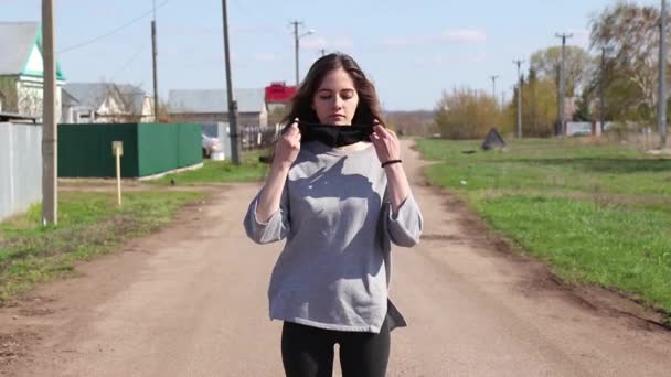 Молодая девушка смотрит в камеру и надевает черную маску в деревне — стоковое видео