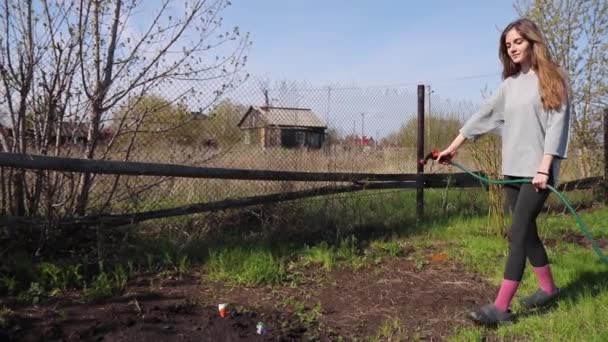 Farmer girl goes to the garden beds and watering them with a garden spray in the village — Stock Video