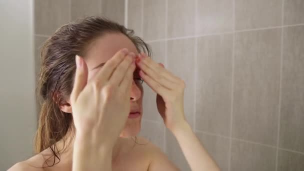 Молодая девушка наносит ягодный скраб на лицо в ванной комнате — стоковое видео