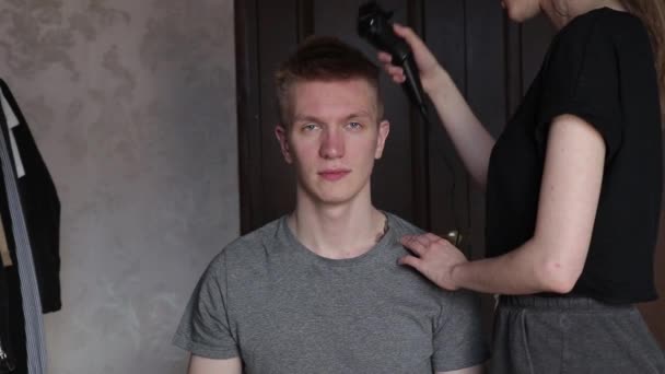 Молода жінка ріже чоловіка, використовуючи затискач для волосся вдома під час ізоляції — стокове відео