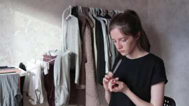 Kadın evde tırnak törpüsüyle tırnak törpülüyor. Arka planda giysiler var. 