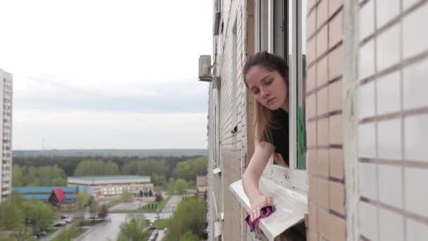 Женщина моет подоконник возле жилого дома — стоковое видео