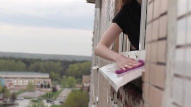 Kadın bir apartmanın penceresini temizliyor.