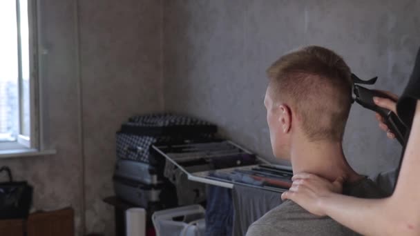Молодая женщина стрижет мужчину с помощью стрижки волос дома во время изоляции вид сзади — стоковое видео